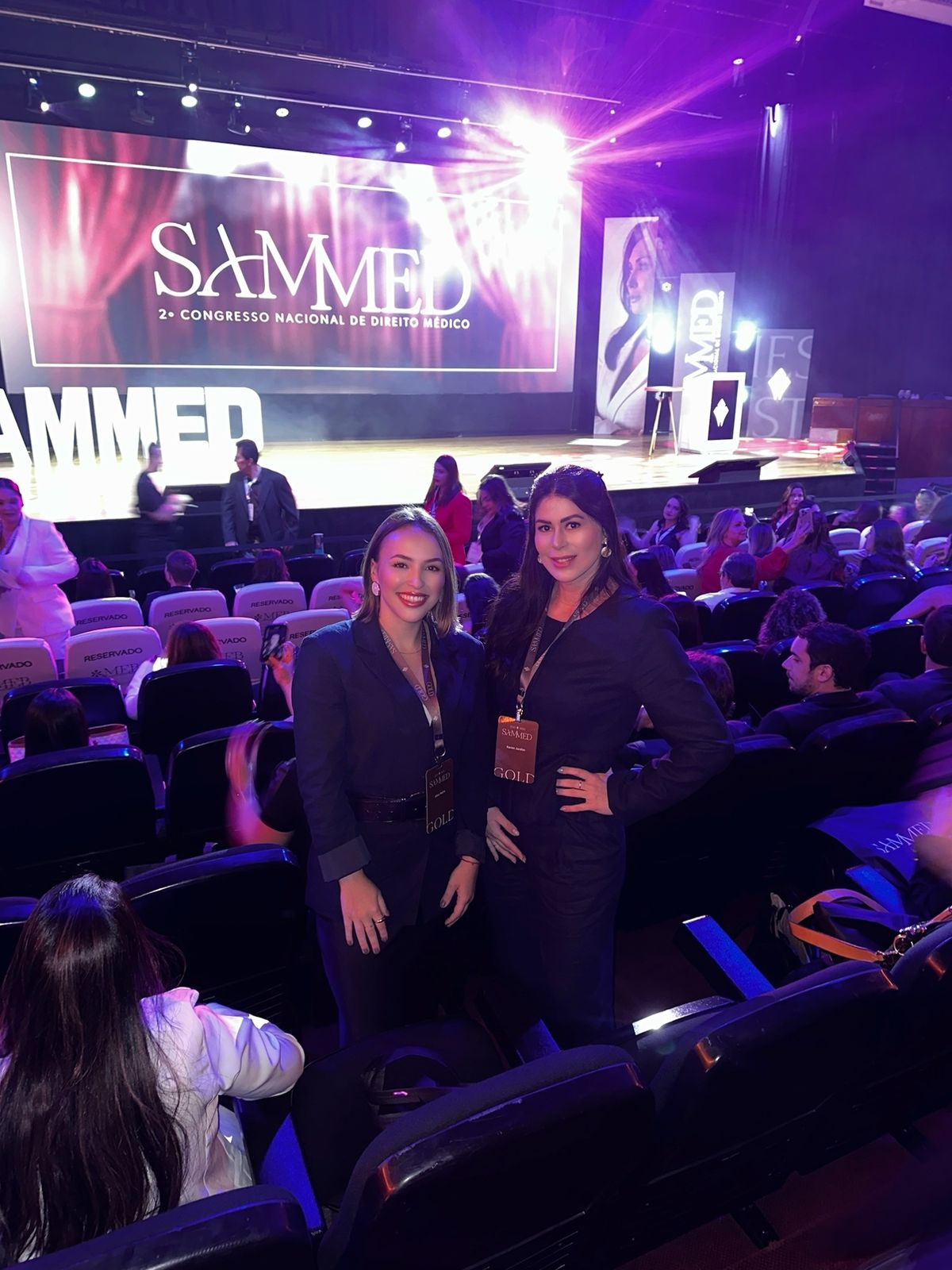 Dra. Karen Batista Jardim e outra participante durante o 2º Congresso Nacional de Direito Médico, em auditório iluminado com palco do evento ao fundo.