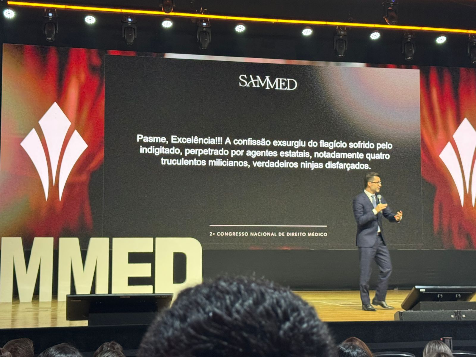 Palestrante no palco do 2º Congresso Nacional de Direito Médico apresentando caso jurídico enquanto o público acompanha a exposição.